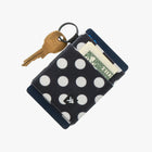 Black polka dot wallet with a key and dollar bill on a white background