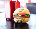 Plush toy resembling a hamburger with text on a table