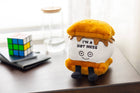 Plush toy resembling a hot mess with text on a desk next to a Rubik's cube