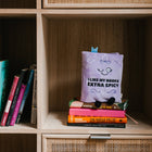 Stack of books with a purple book titled 'I Like My Books Extra Spicy' on a wooden shelf.
