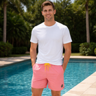 Man wearing a white t-shirt and pink shorts standing by a pool.