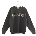 Black sweatshirt with 'CALIFORNIA' text on a hanger against a beige wall.