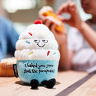 Plush toy resembling a ice cream cone with text on a table with people in the background.