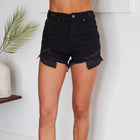 Model wearing black denim shorts standing on a wooden floor with a white wall background