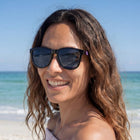 Woman wearing sunglasses on a beach with clear blue sky and ocean.