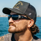 Man wearing a black cap and sunglasses with a body of water in the background