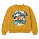 A mustard yellow crewneck sweatshirt featuring a retro-style circular graphic of Santa Monica, California, with palm trees, a pier, beach, and the text 'Santa Monica California' in white script.
