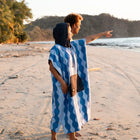 Two people on a beach, one wearing a Nomadix - Changing Poncho: Slack Tide Coastal Blue, pointing towards the ocean.