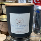 Black candle with a wooden lid labeled 'Santa Monica, California' on a store shelf.