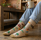 Person wearing socks with tree designs, sitting on a wooden floor holding a mug.