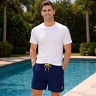 Man wearing a white t-shirt and navy shorts with yellow drawstring by a pool.