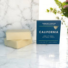 Bar of soap and blue packaging on a marble surface with flowers in the background