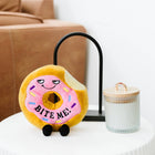 Plush donut toy with a face on a white surface next to a glass jar.