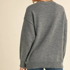 A woman shown from the back wearing a heather gray knit sweater and blue jeans against a plain beige studio background.