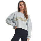 Woman wearing a gray sweatshirt with 'California' text, black shorts, and white sneakers on a plain background