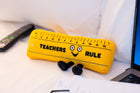 Plush toy shaped like a ruler with a face, labeled 'Teachers Rule', on a desk.