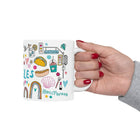 Hand holding a mug with colorful illustrations and text on a white background