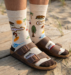 Person wearing socks with California-themed designs and brown sandals on a sandy background