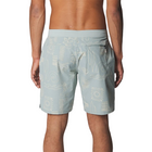 A man wearing light blue board shorts with a white tropical beach-themed print, shown from the back against a light gray studio background.