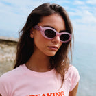 Woman wearing pink sunglasses and a pink t-shirt with text, standing outdoors.