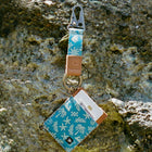Keychain with card holder attached, featuring a blue and white pattern, on a textured stone surface.