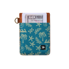 A teal canvas cardholder wallet with a cream palm tree and starfish pattern, brown leather trim, and a gold-tone key ring, shown with a card partially inserted. A small black logo patch is visible on the front.