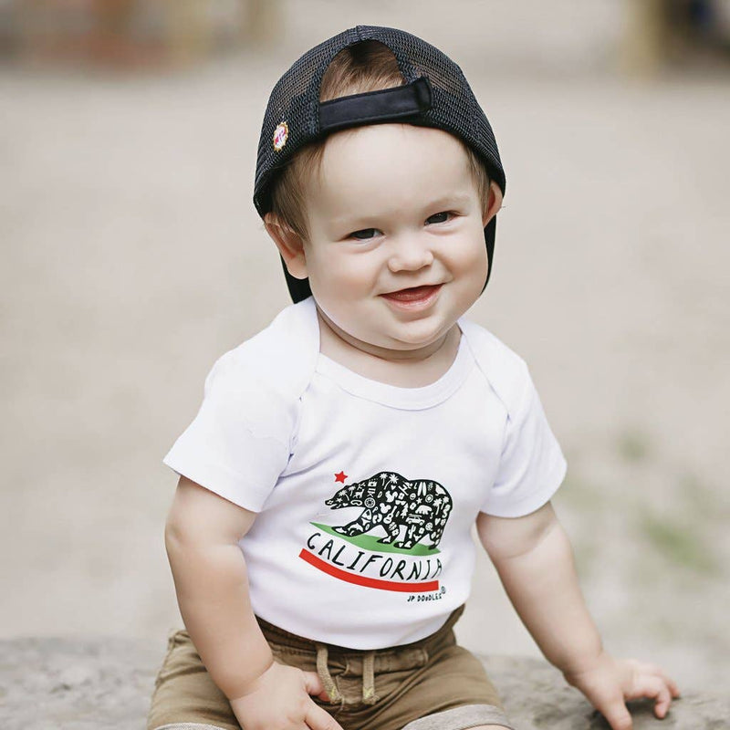Baby wearing a white t-shirt with a California bear design and a black cap.