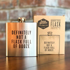 Metallic flask with humorous text next to its packaging on a wooden surface.