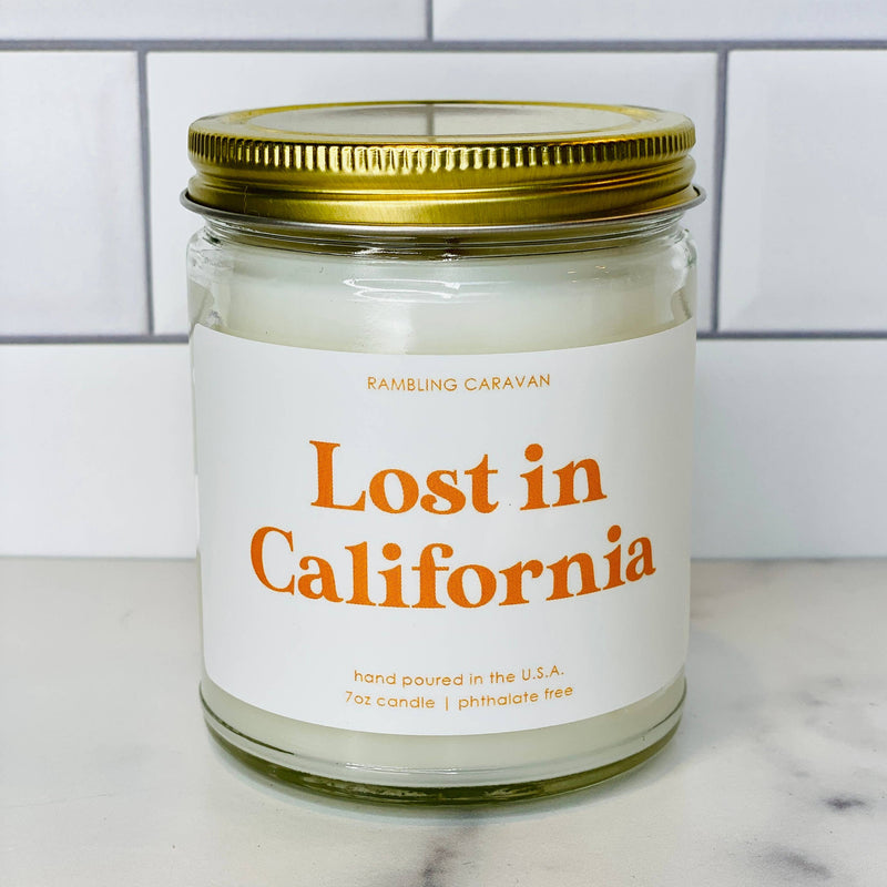 Candle jar labeled 'Lost in California' on a marble surface with a tiled wall background