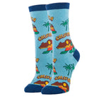 A pair of light blue crew socks with a California-themed graphic print featuring palm trees, mountains, and the word 'CALIFORNIA' in yellow, green, and orange, with dark blue ribbed cuffs, heels, and toes.