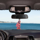 Car dashboard with a rearview mirror and a pink car air freshener hanging from it, with a scenic view outside.