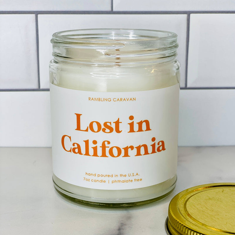 Candle jar labeled 'Lost in California' on a marble surface with a tiled wall background