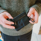 Person holding a black zippered pouch with a carabiner attachment