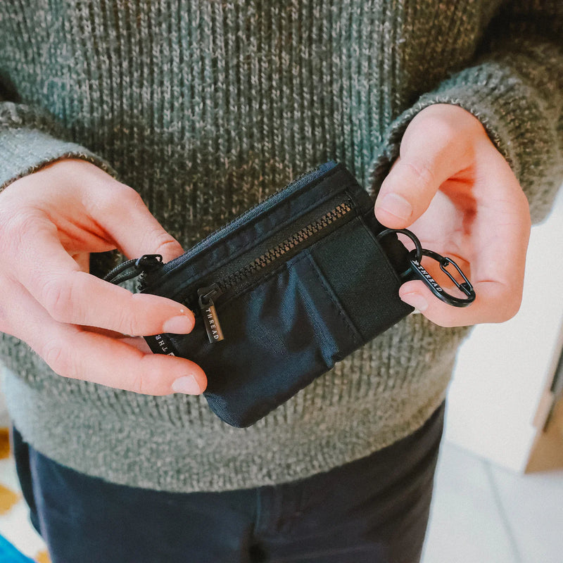 Person holding a black zippered pouch with a carabiner attachment