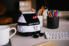 Plush toy resembling a milk carton with text on a desk with stationery items.