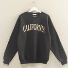 Black sweatshirt with 'CALIFORNIA' text on a hanger against a beige wall.