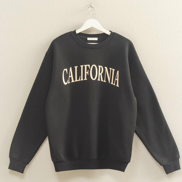 Black sweatshirt with 'CALIFORNIA' text on a hanger against a beige wall.