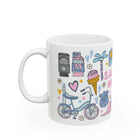 White mug with colorful illustrations including a bicycle, ice cream cone, and houses on a white background