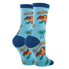 A pair of crew socks with a light blue background featuring a California-themed graphic print of a surfer riding a wave, palm trees, and the word 'CALIFORNIA' in yellow, with dark blue ribbed cuffs, heels, and toes.