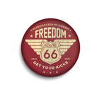 A round pinback button badge magnet featuring a distressed vintage design with the words 'FREEDOM', 'ROUTE 66', 'GET YOUR KICKS', and 'UNITED STATES OF AMERICA'. The badge has a dark red background with a cream-colored graphic and is shown on a clean white background with a soft drop shadow.