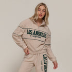 Woman wearing a cream tracksuit with 'Los Angeles California' text on a plain background