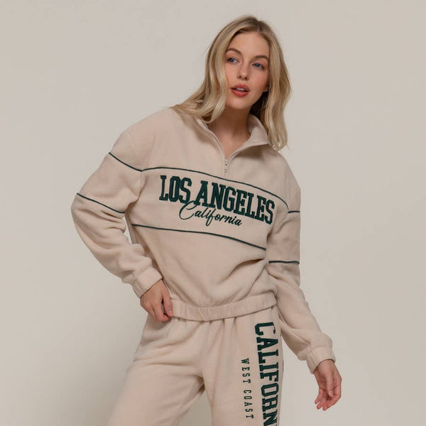 Woman wearing a cream tracksuit with 'Los Angeles California' text on a plain background