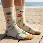 Beige socks with beach-themed designs worn on a wooden platform by the ocean.