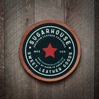 Round leather coaster with 'Sugarhouse Premium Leather Coasters' branding on a wooden background
