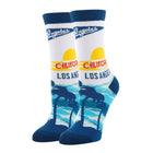 A pair of crew socks featuring a retro California Los Angeles sunset and palm tree graphic. The socks are primarily white with dark blue cuffs, heels, and toes, and include a yellow sun, red 'CALIFORNIA' text, and blue 'Los Angeles' lettering.
