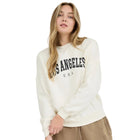 Woman wearing a white sweatshirt with 'Los Angeles USA' text and beige shorts on a white background