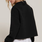 Woman wearing a black jacket and white skirt against a plain background