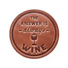 A round brown leather coaster with embossed text reading 'THE ANSWER IS always WINE' and a wine glass illustration, displayed on a dark rustic wooden background.