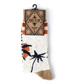 A pair of patterned crew socks hanging from a black plastic hanger against a plain white background. The socks are off-white with a speckled texture, featuring a black palm tree graphic, an orange and black sun motif, and orange and black stripes near the cuff.