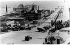 Vintage black and white photograph of a beachfront amusement park with cars and people.